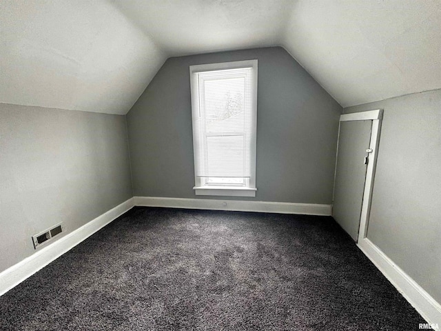 additional living space with dark colored carpet, visible vents, baseboards, and vaulted ceiling