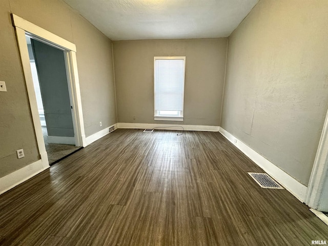 spare room featuring visible vents, baseboards, and dark wood-style flooring