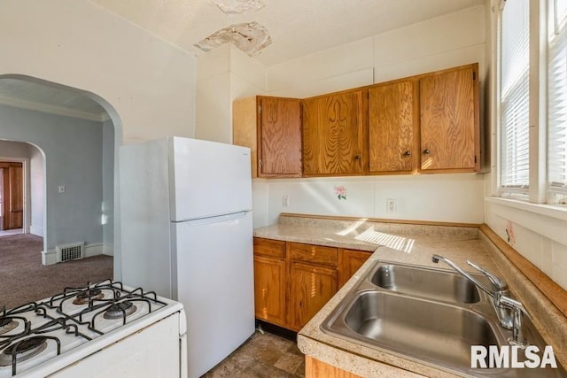 4227 11th St, Rock Island, IL 61201 - kitchen with white appliances, brown cabinetry, arched walkways, and a sink