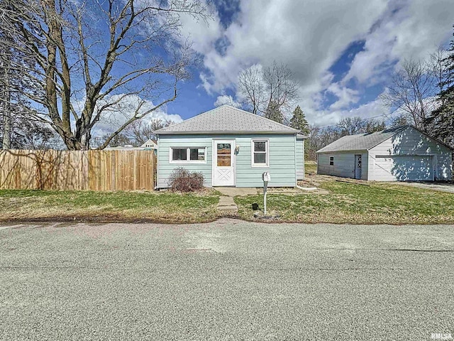 bungalow featuring an outbuilding, a detached garage, fence, and a front lawn