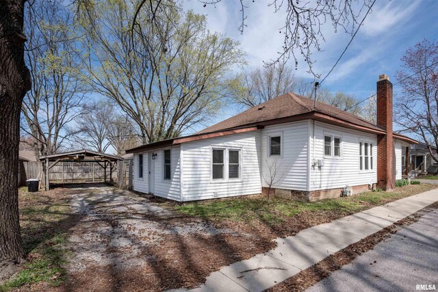 view of property exterior with fence, a detached carport, and a chimney