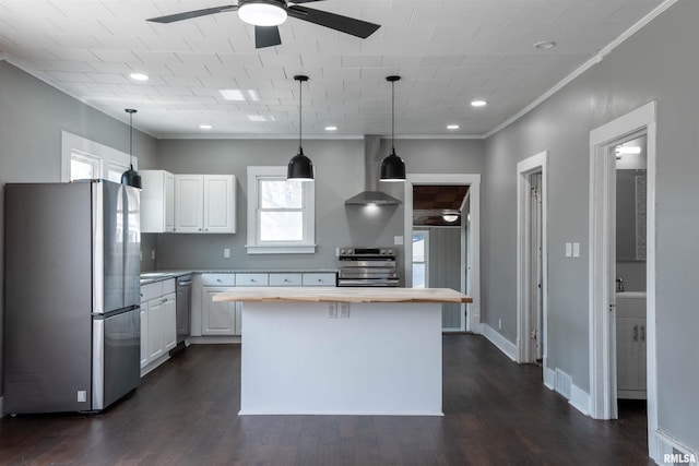 kitchen featuring white cabinetry, wooden counters, a ceiling fan, appliances with stainless steel finishes, and wall chimney exhaust hood