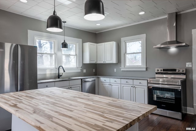 kitchen featuring white cabinetry, butcher block countertops, stainless steel appliances, wall chimney range hood, and ornamental molding