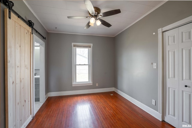 unfurnished bedroom featuring a closet, a barn door, dark wood-style floors, baseboards, and ornamental molding