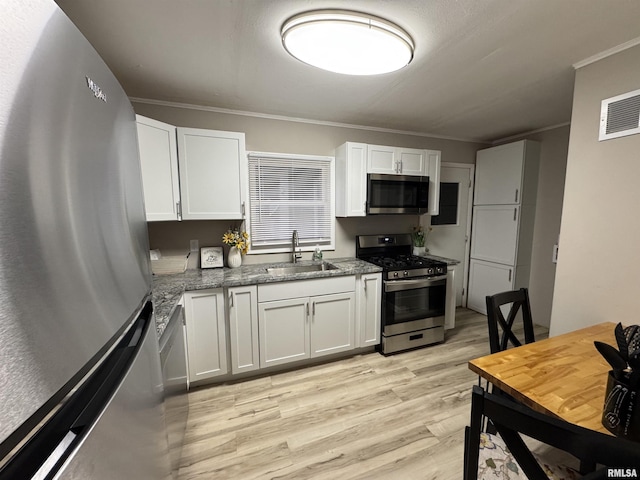 kitchen featuring visible vents, appliances with stainless steel finishes, a sink, ornamental molding, and light wood-style flooring