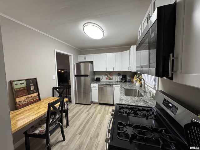 kitchen featuring crown molding, a sink, light wood finished floors, stainless steel appliances, and white cabinetry