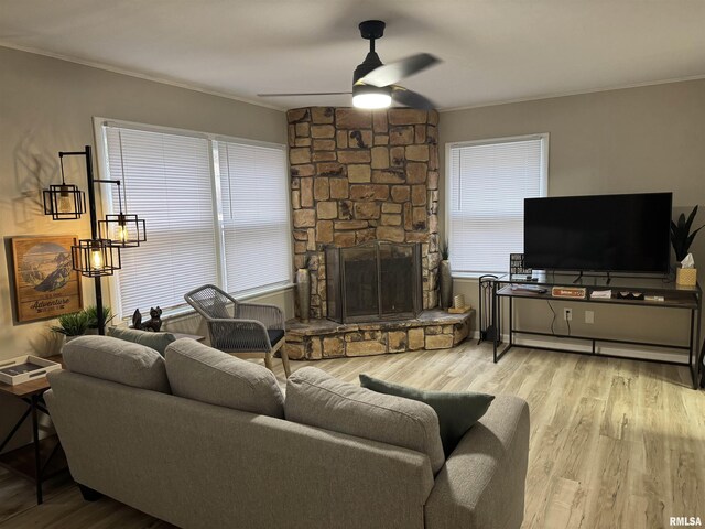 living area with crown molding, a stone fireplace, a ceiling fan, and wood finished floors