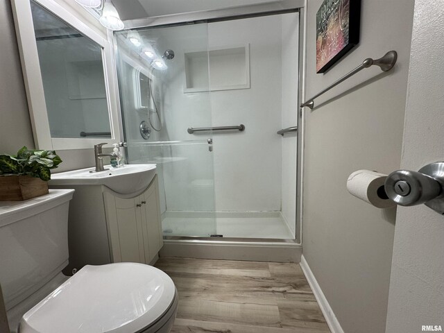 bathroom featuring a stall shower, wood finished floors, vanity, baseboards, and toilet