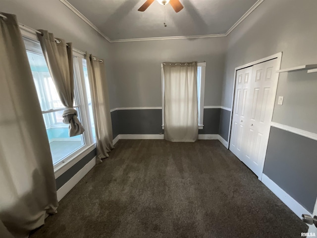 unfurnished bedroom with crown molding, baseboards, dark carpet, a ceiling fan, and a closet