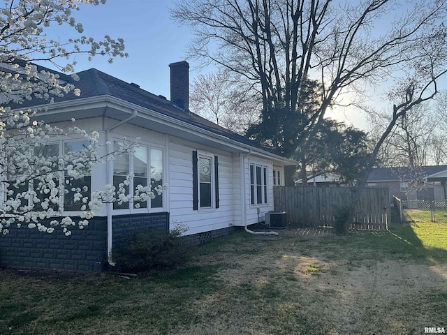 view of home's exterior with a lawn, a chimney, fence, and central AC