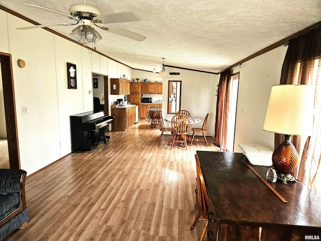 living area with ornamental molding, a textured ceiling, light wood-style flooring, lofted ceiling, and ceiling fan