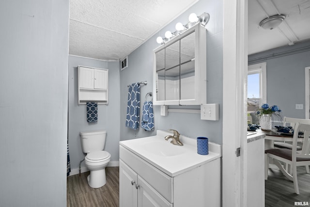 bathroom with vanity, visible vents, toilet, wood finished floors, and baseboards