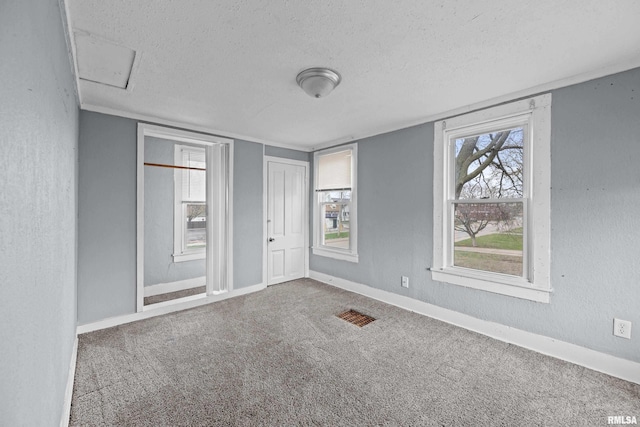 carpeted empty room featuring a textured ceiling, a textured wall, baseboards, and visible vents