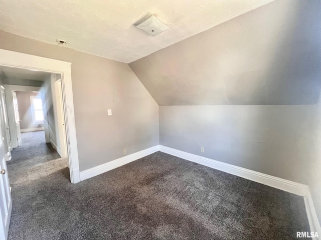bonus room with baseboards, vaulted ceiling, dark colored carpet, and a textured ceiling