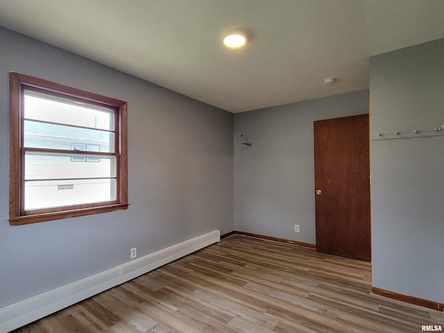 spare room featuring a baseboard radiator, baseboards, and light wood finished floors