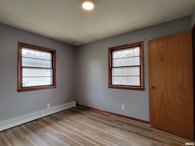 unfurnished room featuring light wood finished floors, baseboards, a baseboard heating unit, and a textured ceiling