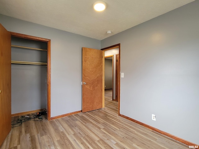 unfurnished bedroom with baseboards, a textured ceiling, a closet, and light wood-style floors