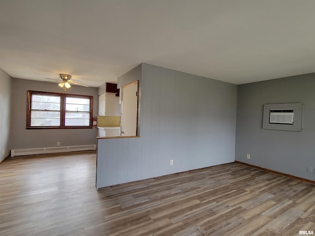 unfurnished room with a baseboard heating unit, an AC wall unit, baseboards, light wood-style floors, and ceiling fan