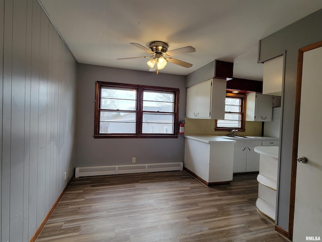 kitchen featuring light countertops, a ceiling fan, white cabinets, light wood-style floors, and a baseboard heating unit