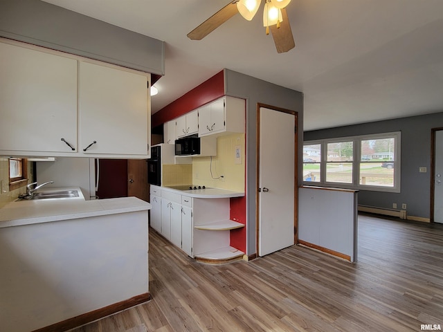 kitchen with light countertops, light wood finished floors, a baseboard radiator, a sink, and black appliances
