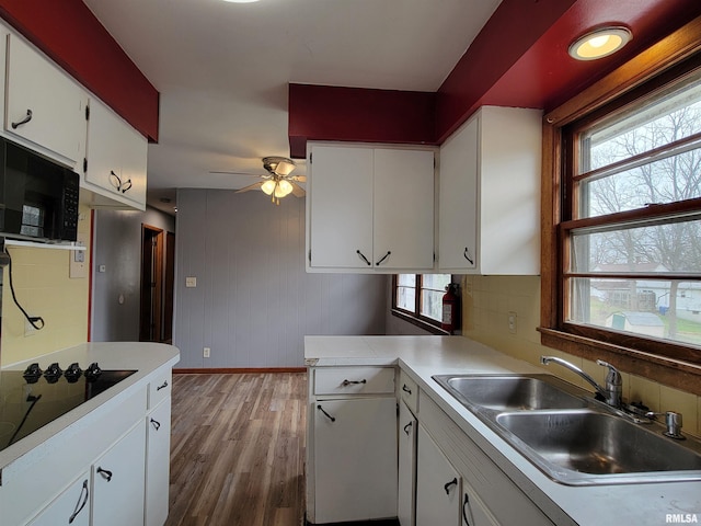 kitchen with white cabinets, light countertops, a sink, light wood-style floors, and black appliances