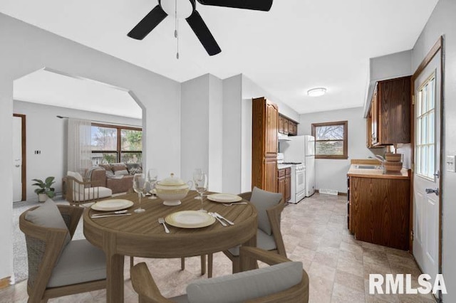dining space with arched walkways, baseboards, a healthy amount of sunlight, and ceiling fan