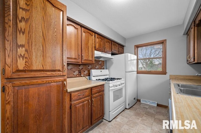kitchen with a sink, light countertops, gas range gas stove, and under cabinet range hood