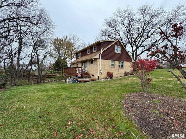 view of side of home with a yard, brick siding, and a wooden deck