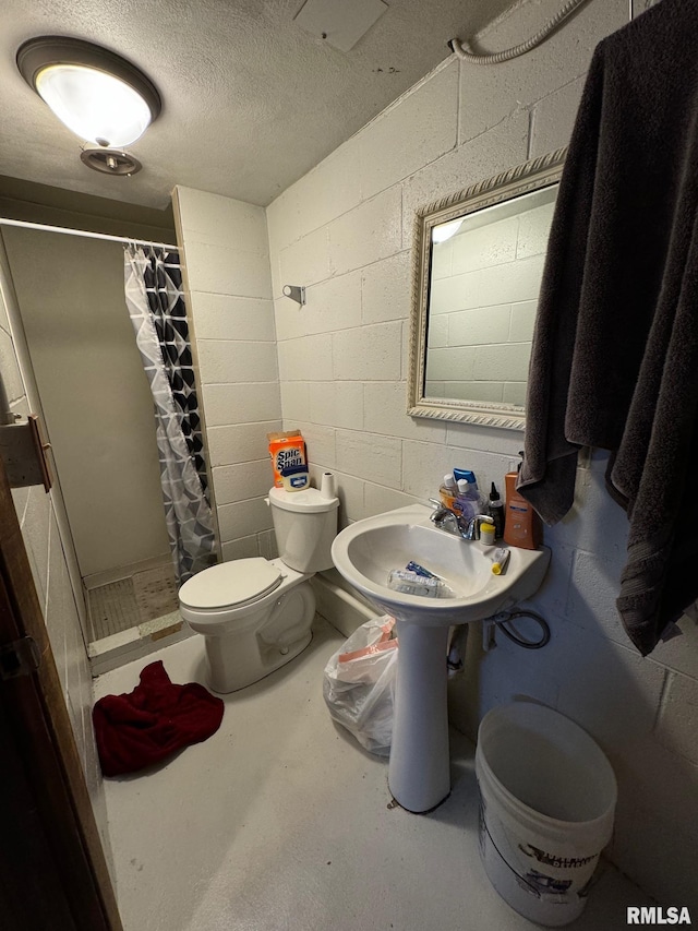 full bathroom featuring a textured ceiling, toilet, a sink, concrete block wall, and a stall shower