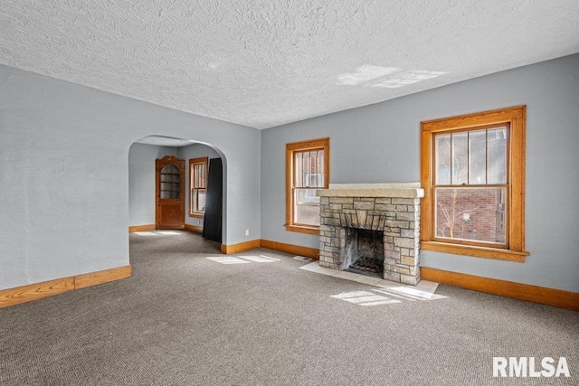 unfurnished living room with baseboards, carpet flooring, arched walkways, and a fireplace