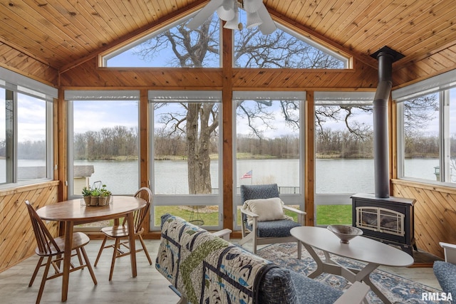 sunroom / solarium featuring a wood stove, a water view, a ceiling fan, vaulted ceiling, and wood finished floors