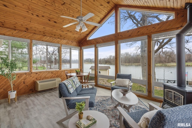 sunroom / solarium featuring a wood stove, a wall mounted AC, healthy amount of natural light, a water view, and high vaulted ceiling