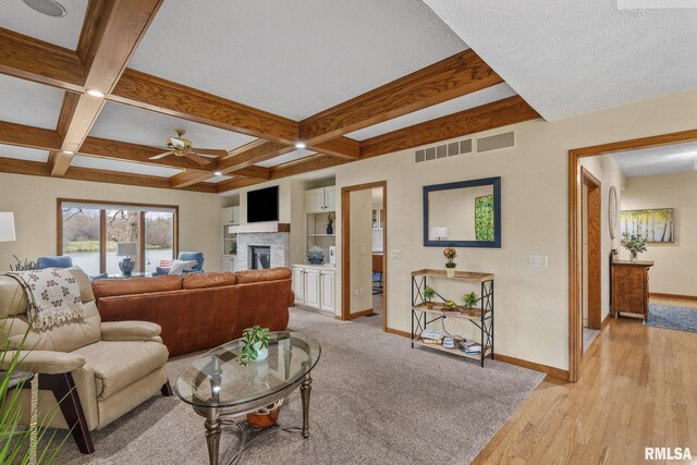 living area featuring baseboards, a ceiling fan, beamed ceiling, a glass covered fireplace, and light wood-style flooring