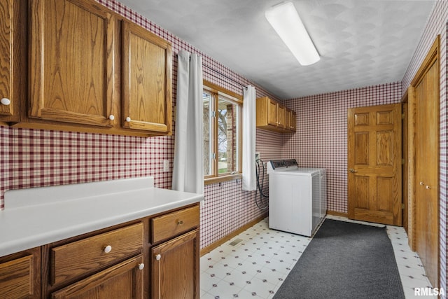 washroom featuring washer / clothes dryer, wallpapered walls, cabinet space, light flooring, and baseboards
