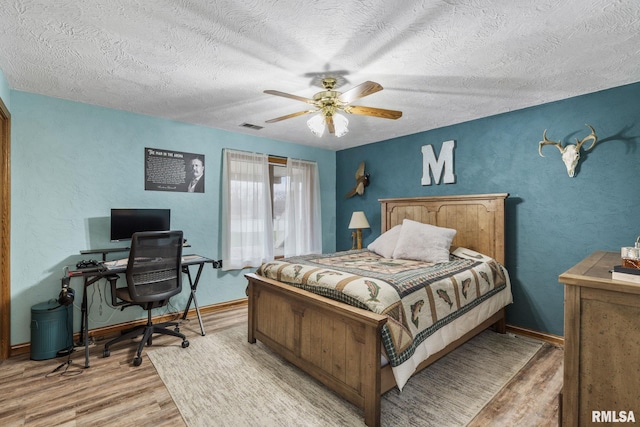 bedroom with light wood finished floors, a textured ceiling, an office area, a ceiling fan, and baseboards