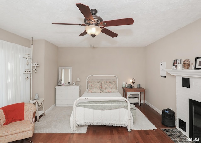 bedroom with wood finished floors, baseboards, and a brick fireplace