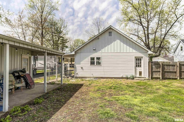 back of house with board and batten siding, a patio area, fence, and a yard