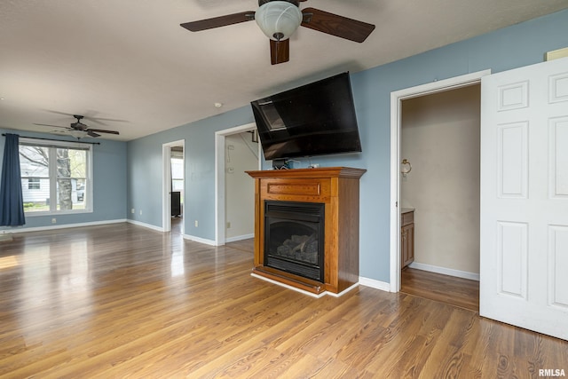 unfurnished living room featuring a glass covered fireplace, light wood-style flooring, baseboards, and a ceiling fan