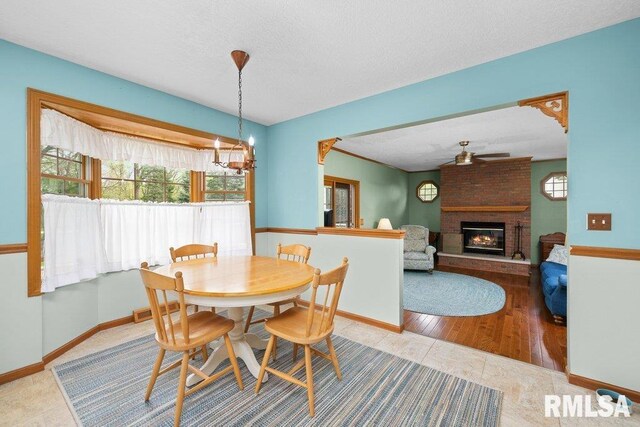 tiled dining area with a healthy amount of sunlight, baseboards, a brick fireplace, and ceiling fan with notable chandelier