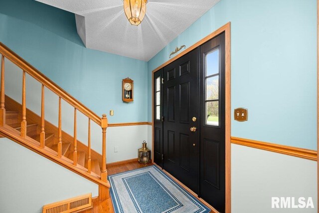 foyer entrance with stairs, baseboards, visible vents, and wood finished floors