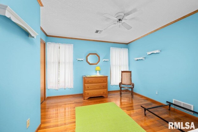 living area featuring visible vents, ornamental molding, a ceiling fan, and wood finished floors