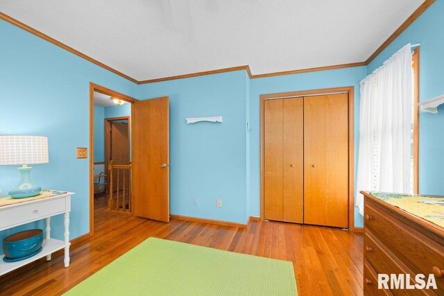 bedroom with a closet, ornamental molding, baseboards, and wood finished floors