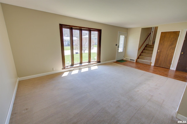 unfurnished living room featuring visible vents, baseboards, carpet, and stairs