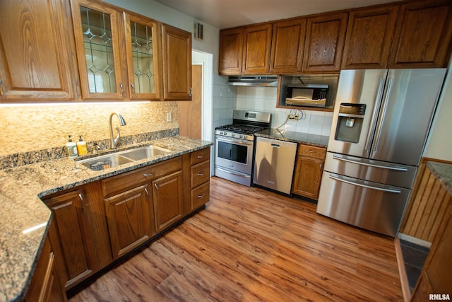 kitchen featuring appliances with stainless steel finishes, under cabinet range hood, a sink, light wood finished floors, and backsplash