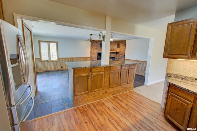 kitchen featuring a brick fireplace, brown cabinets, a wainscoted wall, and stainless steel fridge