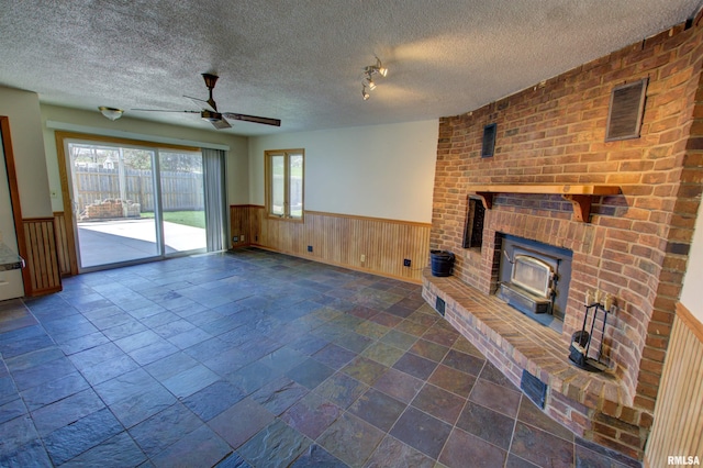 unfurnished living room with a textured ceiling, a ceiling fan, plenty of natural light, and a wainscoted wall