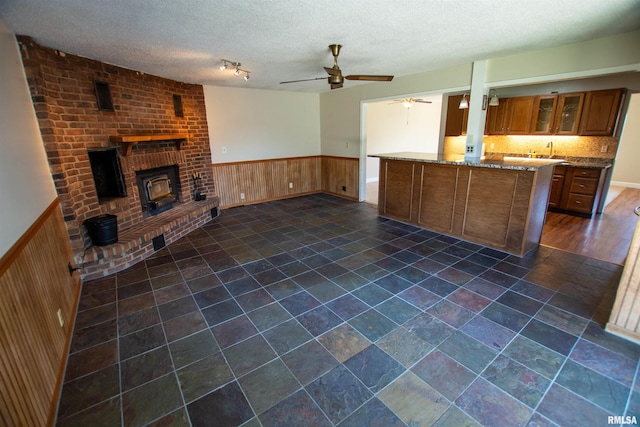kitchen with glass insert cabinets, open floor plan, ceiling fan, brown cabinetry, and wainscoting