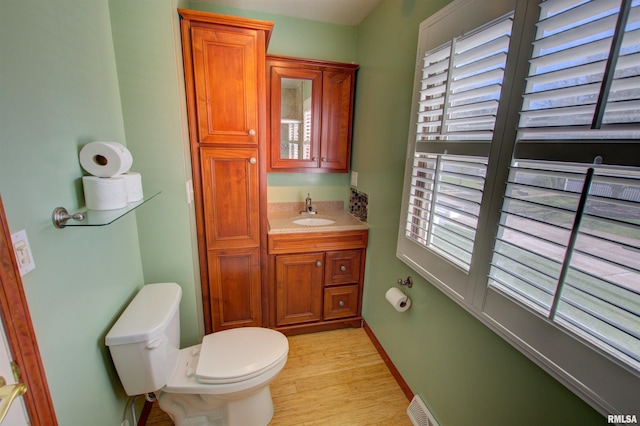 half bath featuring visible vents, toilet, vanity, and wood finished floors