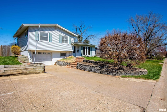 tri-level home with an attached garage, concrete driveway, and fence