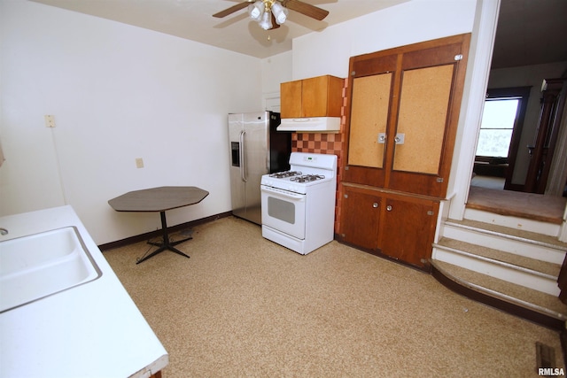 kitchen featuring white gas range oven, a ceiling fan, under cabinet range hood, a sink, and stainless steel fridge